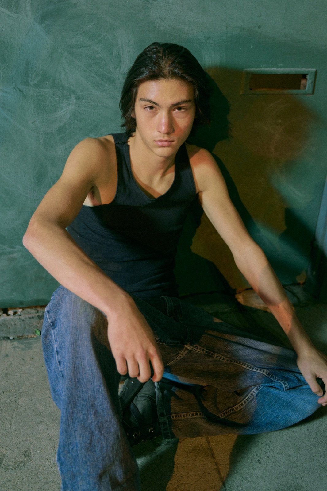 Black tank, seated against a teal wall